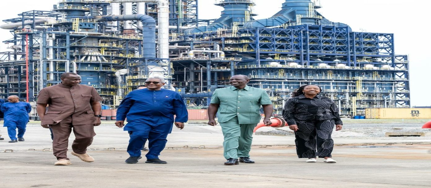 Officials walk in front of a large industrial refinery complex