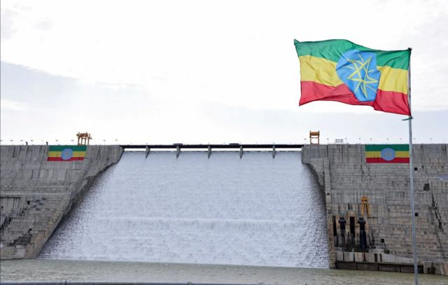 Water pours over the spillway of a large dam with an Ethiopian flag flying beside it