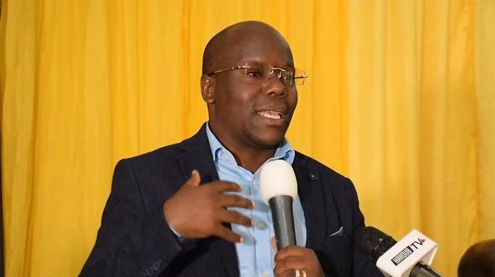 A man in a suit speaks into microphones at a press event
